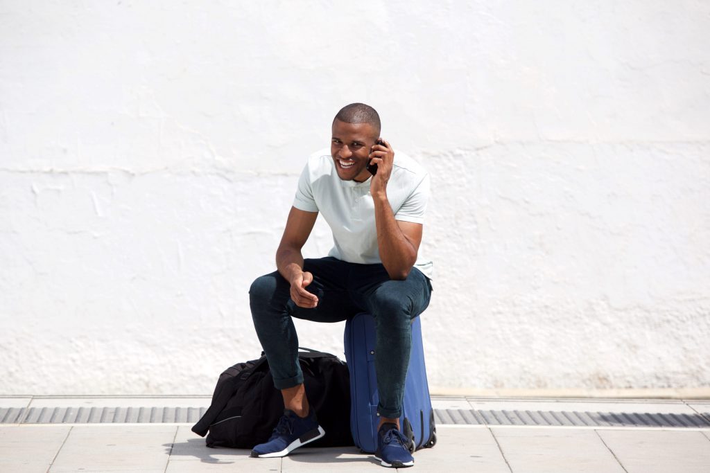 Full body portrait of african american traveler sitting and talking on cellphone