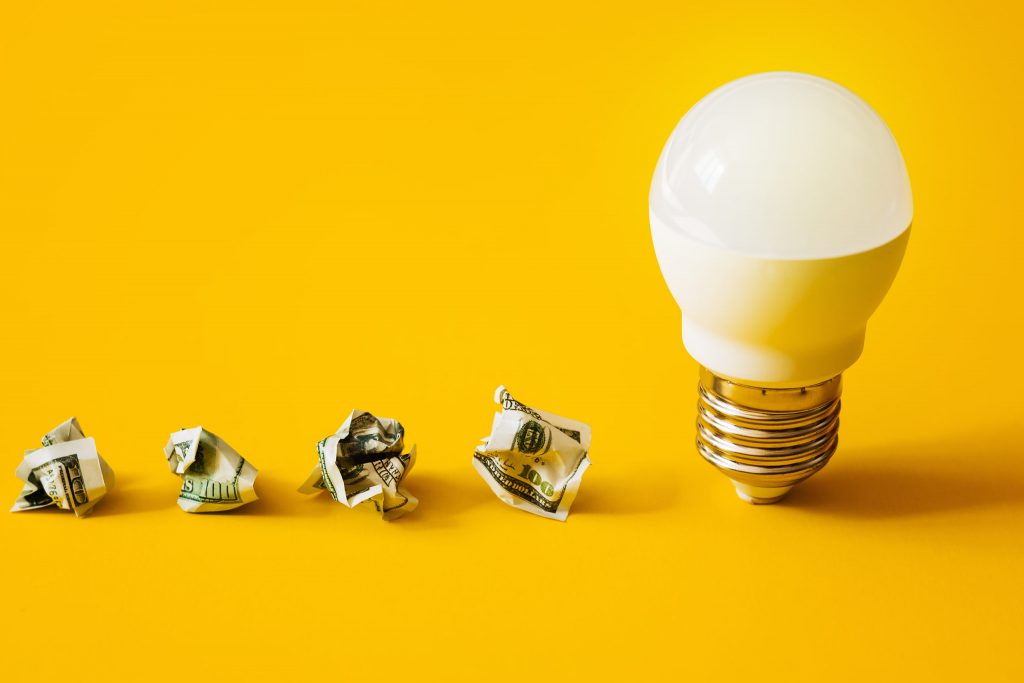 Saving money concept. Lamp and crumpled money in a row on a yellow background.
